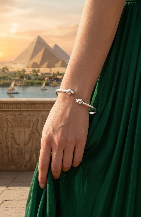 Person wearing a silver cat bracelet with a scenic view of pyramids and a river in the background
