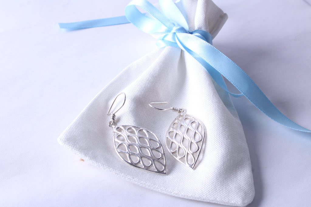 Sterling silver leaf dangle earrings with openwork pattern on a white gift pouch
