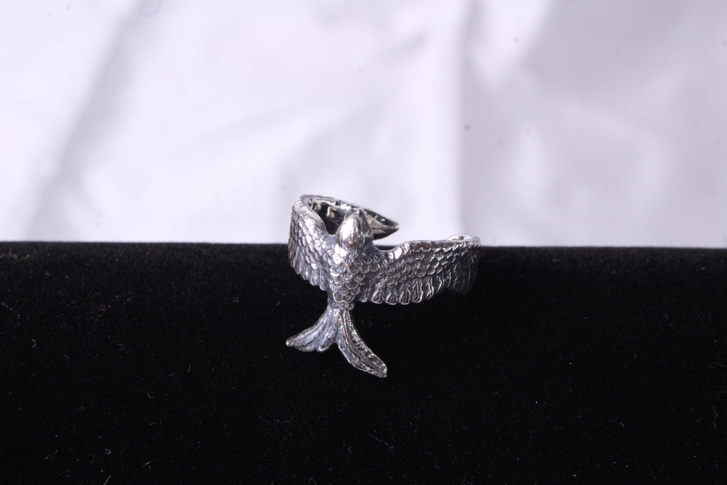 A detailed shot of a silver ring with an anatomically accurate silhouette of a bird. High detail of the metal and mirror polish on a contrasting black background.