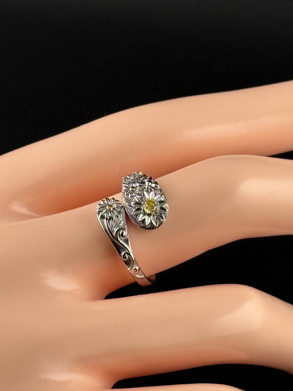 Adjustable sterling silver floral ring with yellow zircon shown on a display hand