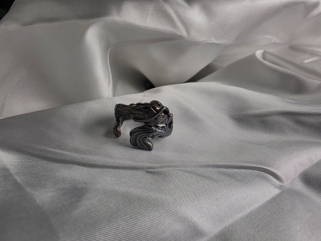 Artisan silver dragon ring with detailed scales and black oxidation on a white silk fabric background.