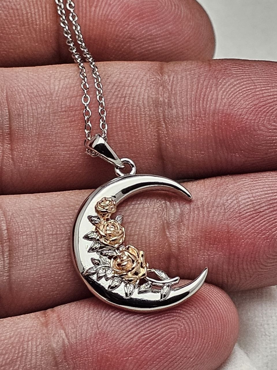 Crescent moon rose 925 sterling silver necklace held by hand to show pendant size and details.