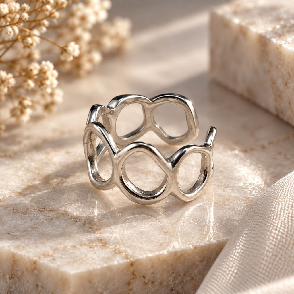 Adjustable sterling silver ring with flowing open circle design on a neutral stone background