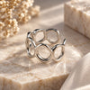 Adjustable sterling silver ring with flowing open circle design on a neutral stone background