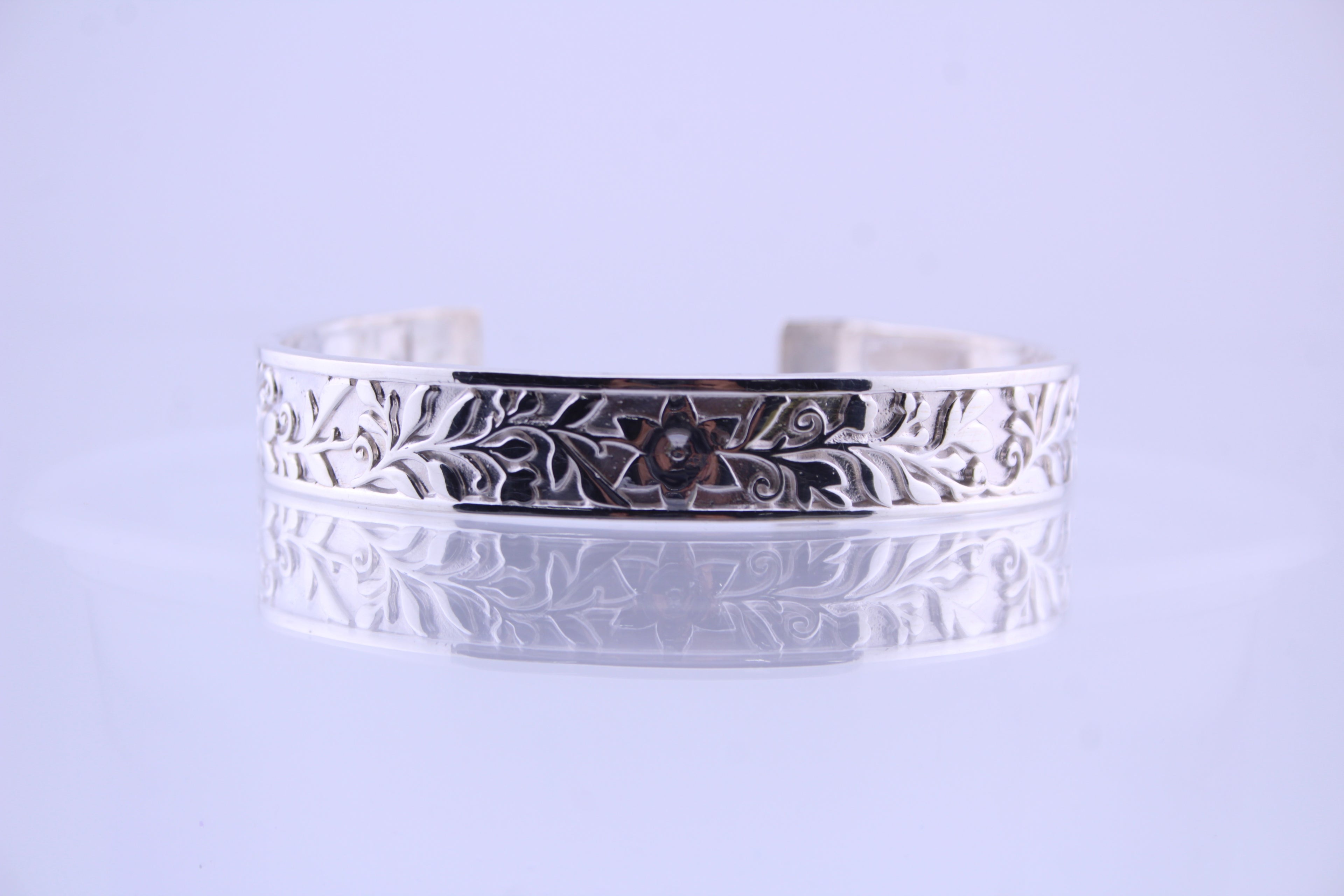 "Front view of the royal blossom silver cuff bracelet lying horizontally with a clear mirror reflection, showcasing the floral flower pattern on a clean white background — luxury 925 sterling silver jewelry."