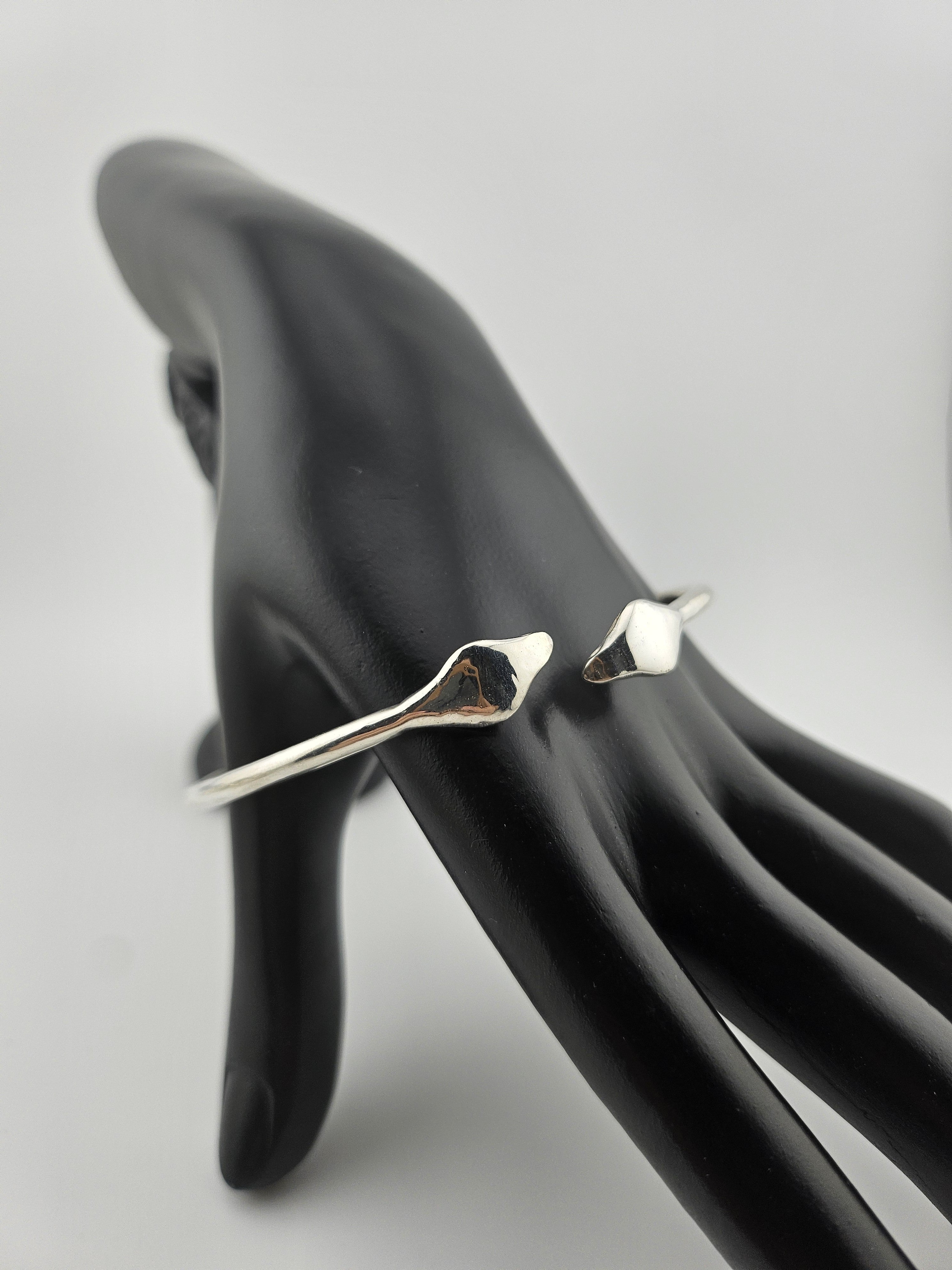"Silver twin cobra cuff bracelet displayed on a black mannequin hand, featuring two detailed snake heads on a clean light background."