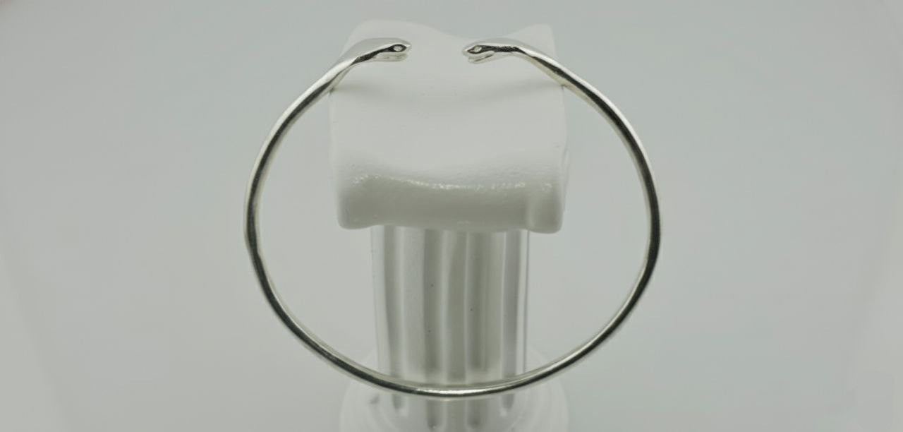 "Side view of a silver twin cobra cuff bracelet with two sculpted snake heads on a white background."