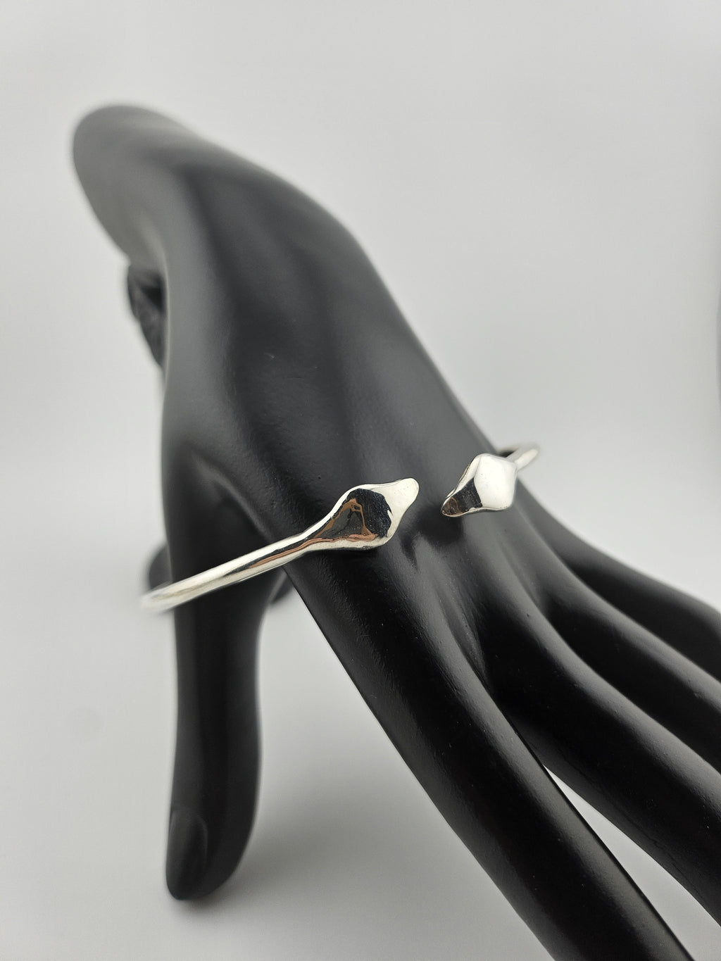 "Sterling silver cuff bracelet displayed on a black mannequin hand, featuring a sculpted twin-head design on a clean light background."

