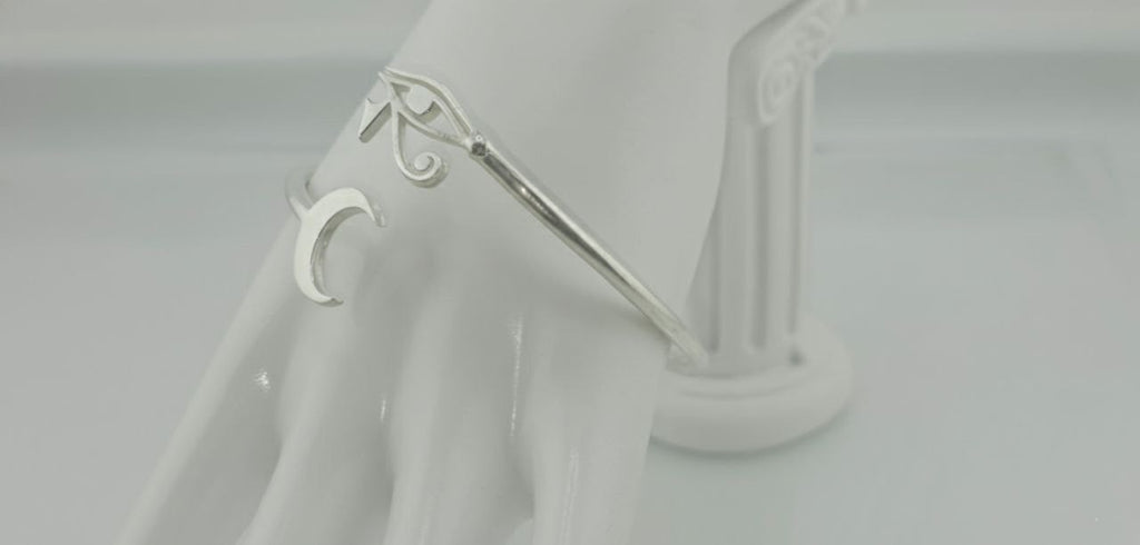 sterling silver cuff bracelet with engraved eye and crescent moon, displayed on a clear stand, side-angle view