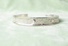 Minimalist silver cuff bracelet with moon and star symbols isolated on a soft light green background, showcasing smooth edges and premium polishing.
