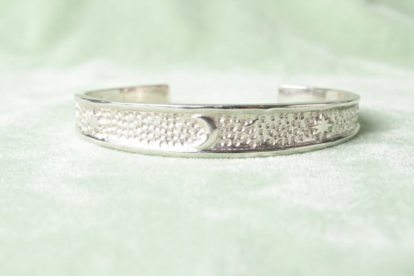 Minimalist silver cuff bracelet with moon and star symbols isolated on a soft light green background, showcasing smooth edges and premium polishing.