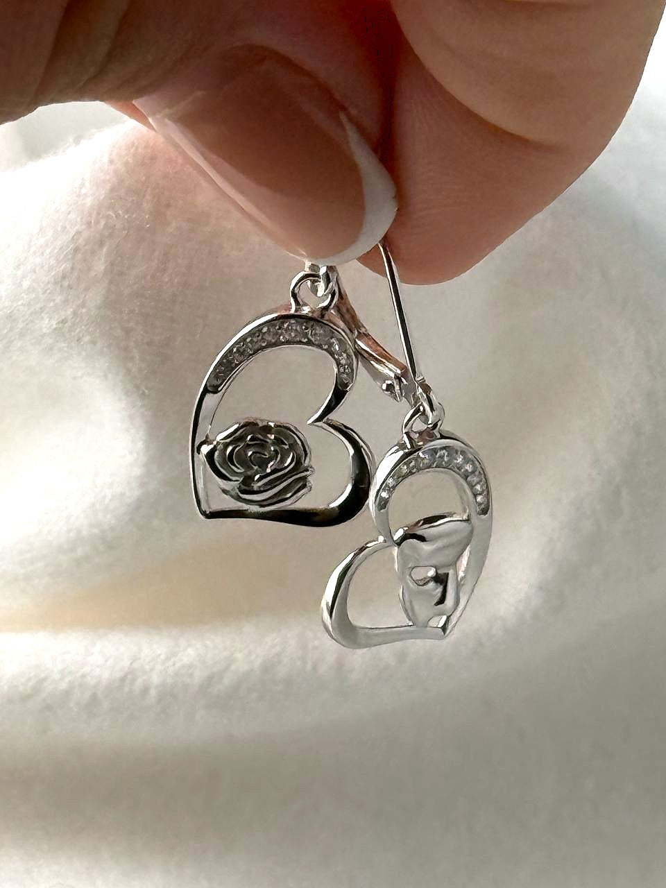 Close-up of sterling silver heart earrings with rose and masquerade mask details and cubic zirconia accents