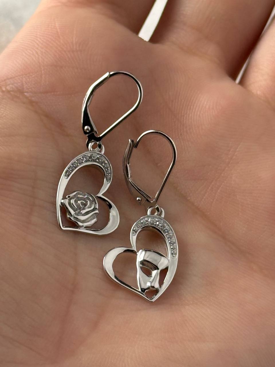 Sterling silver rose and masquerade heart earrings with cubic zirconia accents shown in hand for scale