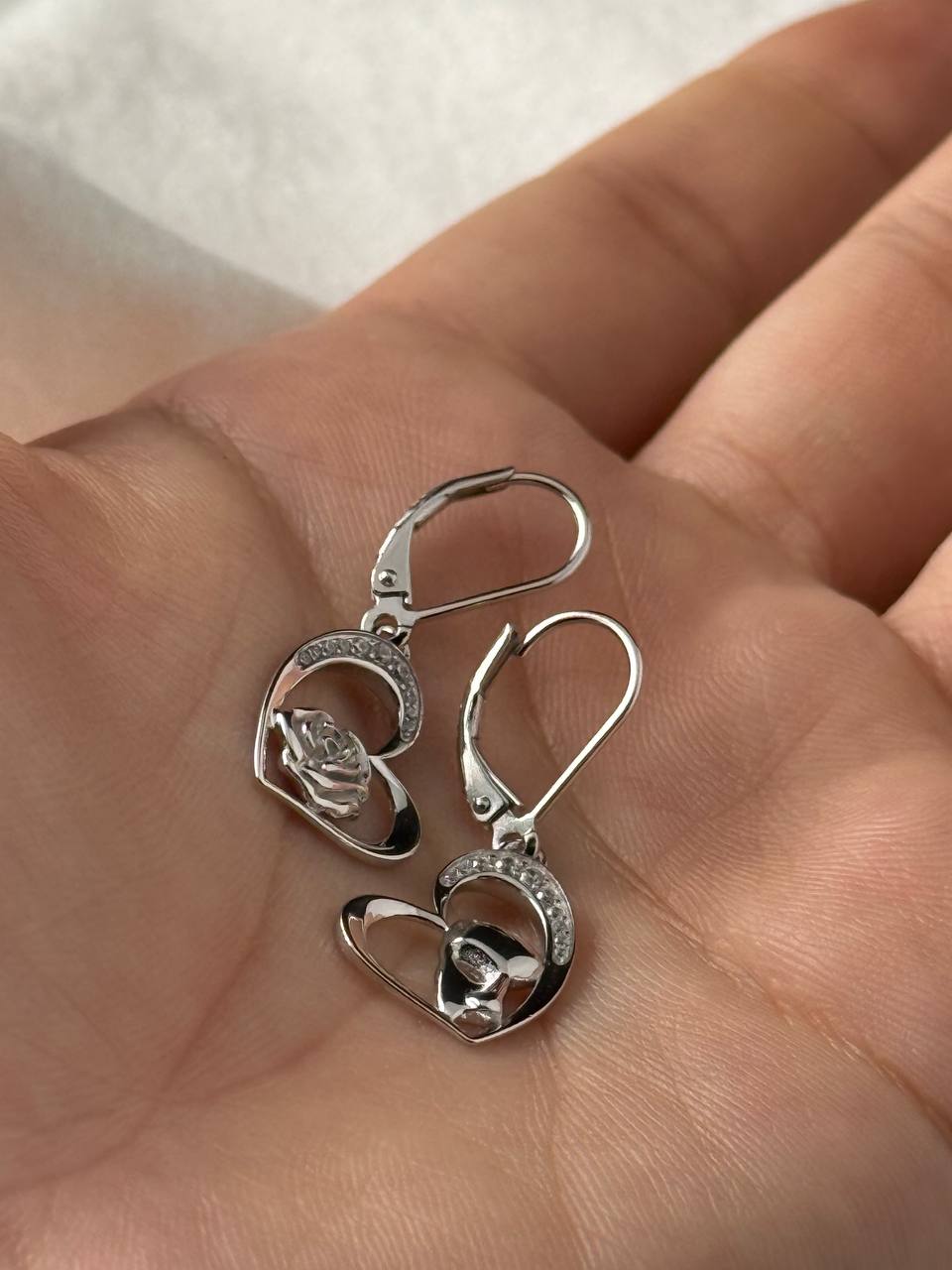 Sterling silver rose and masquerade heart earrings with cubic zirconia accents shown in hand