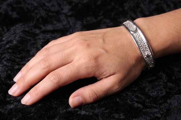 A heavy sterling silver cuff bracelet titled Moon Scattering worn on a wrist, featuring detailed celestial engraving and a high-mirror polish finish