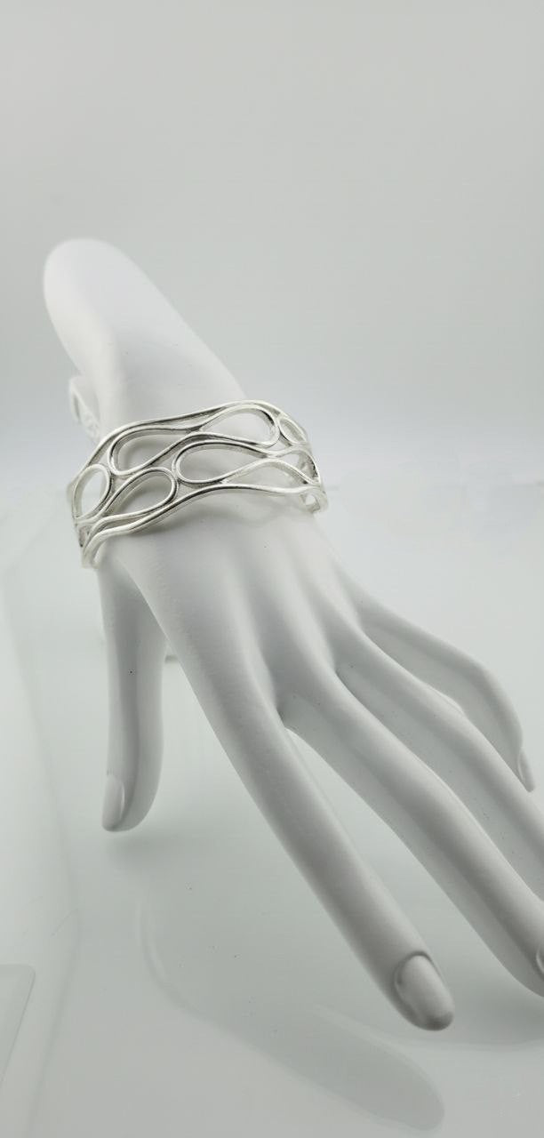 Silver infinity wave cuff bracelet displayed on a white mannequin hand.