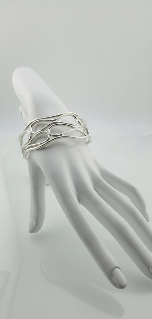 Silver infinity wave cuff bracelet displayed on a white mannequin hand.