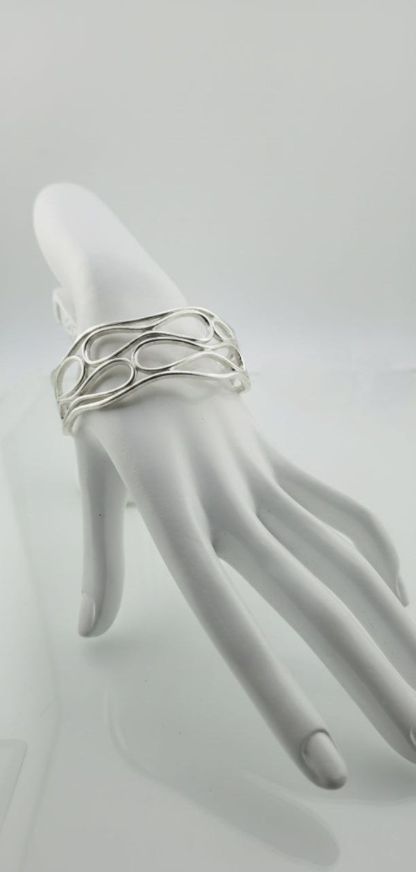 Silver infinity wave cuff bracelet displayed on a white mannequin hand.