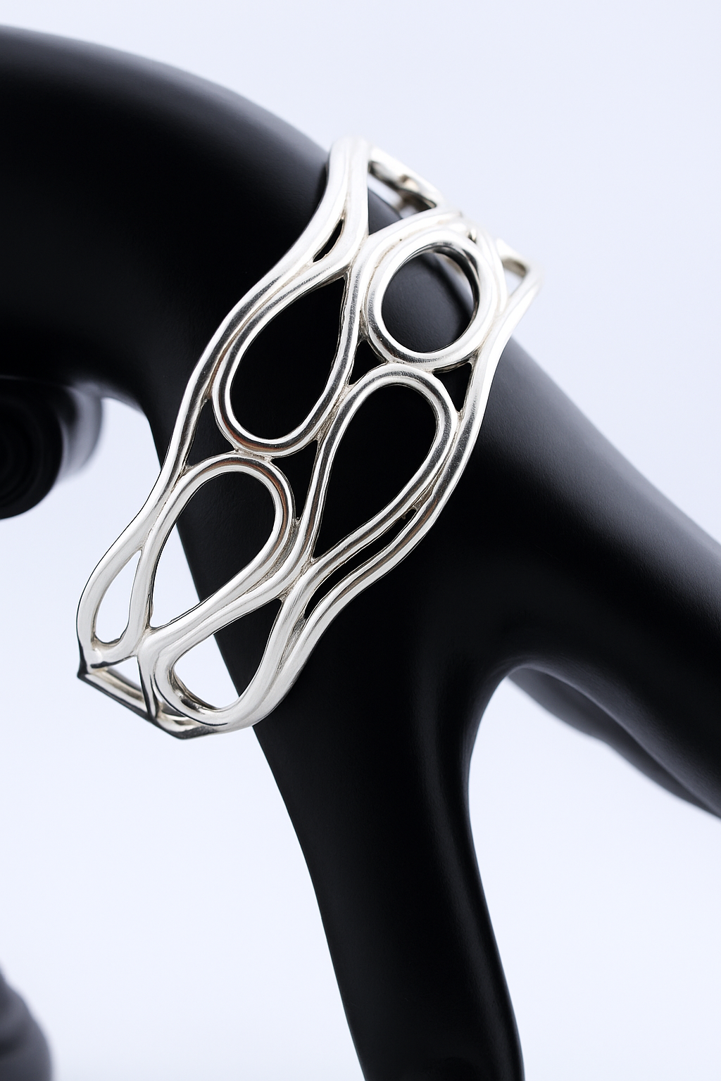 Silver openwork infinity cuff bracelet displayed on a black mannequin arm.
