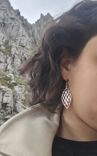 Sterling silver leaf earring worn by a woman, shown in a natural outdoor setting
