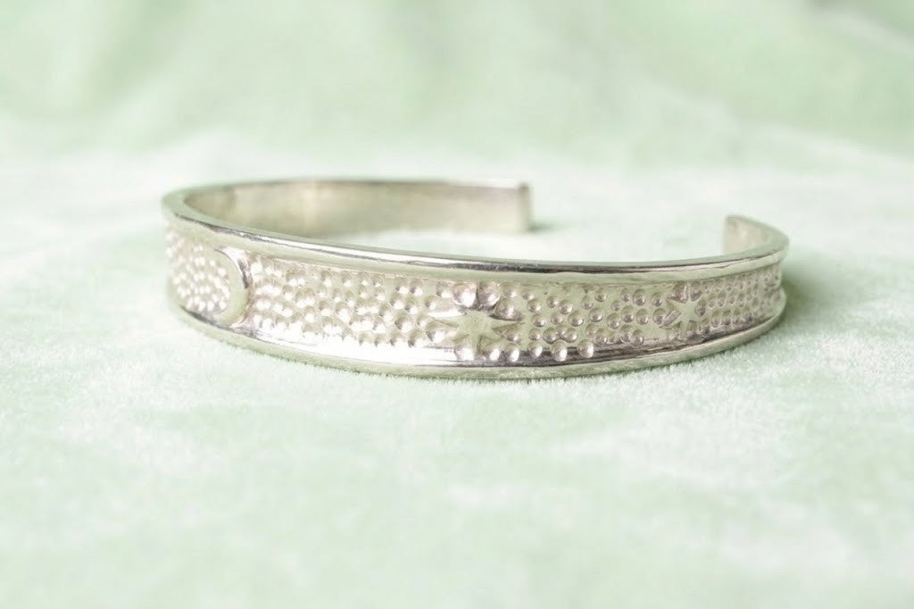 Perspective view of a 35g sterling silver cuff on a dark textured surface, highlighting the contrast between the polished silver and the celestial relief.