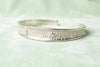 Perspective view of a 35g sterling silver cuff on a dark textured surface, highlighting the contrast between the polished silver and the celestial relief.