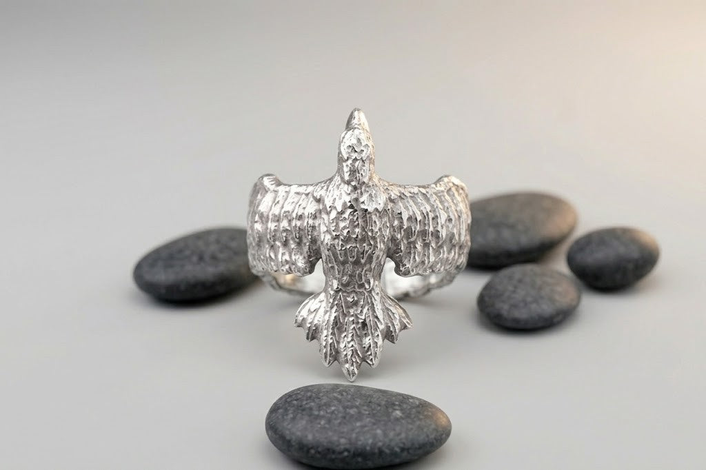 Unisex ring 'Raven' made of polished silver. A symbol of wisdom and heritage in a modern jewelry design. Composition with stones on a gray background.