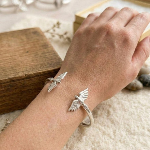 Handcrafted 925 sterling silver cuff bracelet featuring "Twin Wings" sculpted birds design. Minimalist heritage jewelry with high-polish finish shown on a wrist.