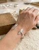 Handcrafted 925 sterling silver cuff bracelet featuring "Twin Wings" sculpted birds design. Minimalist heritage jewelry with high-polish finish shown on a wrist.
