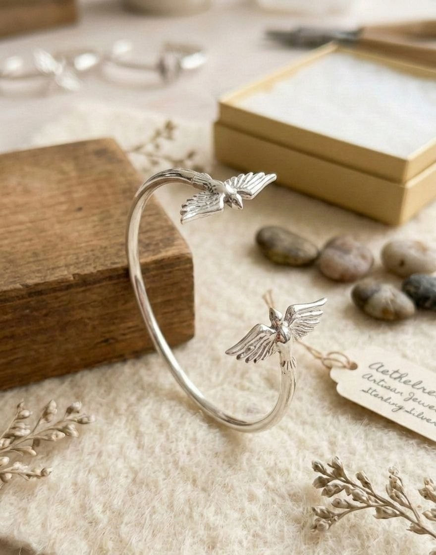 Artistic display of the Twin Wings 925 sterling silver cuff bracelet on a wooden background with heritage-style packaging. High-end handcrafted jewelry by Lakseena.