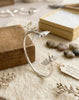Artistic display of the Twin Wings 925 sterling silver cuff bracelet on a wooden background with heritage-style packaging. High-end handcrafted jewelry by Lakseena.